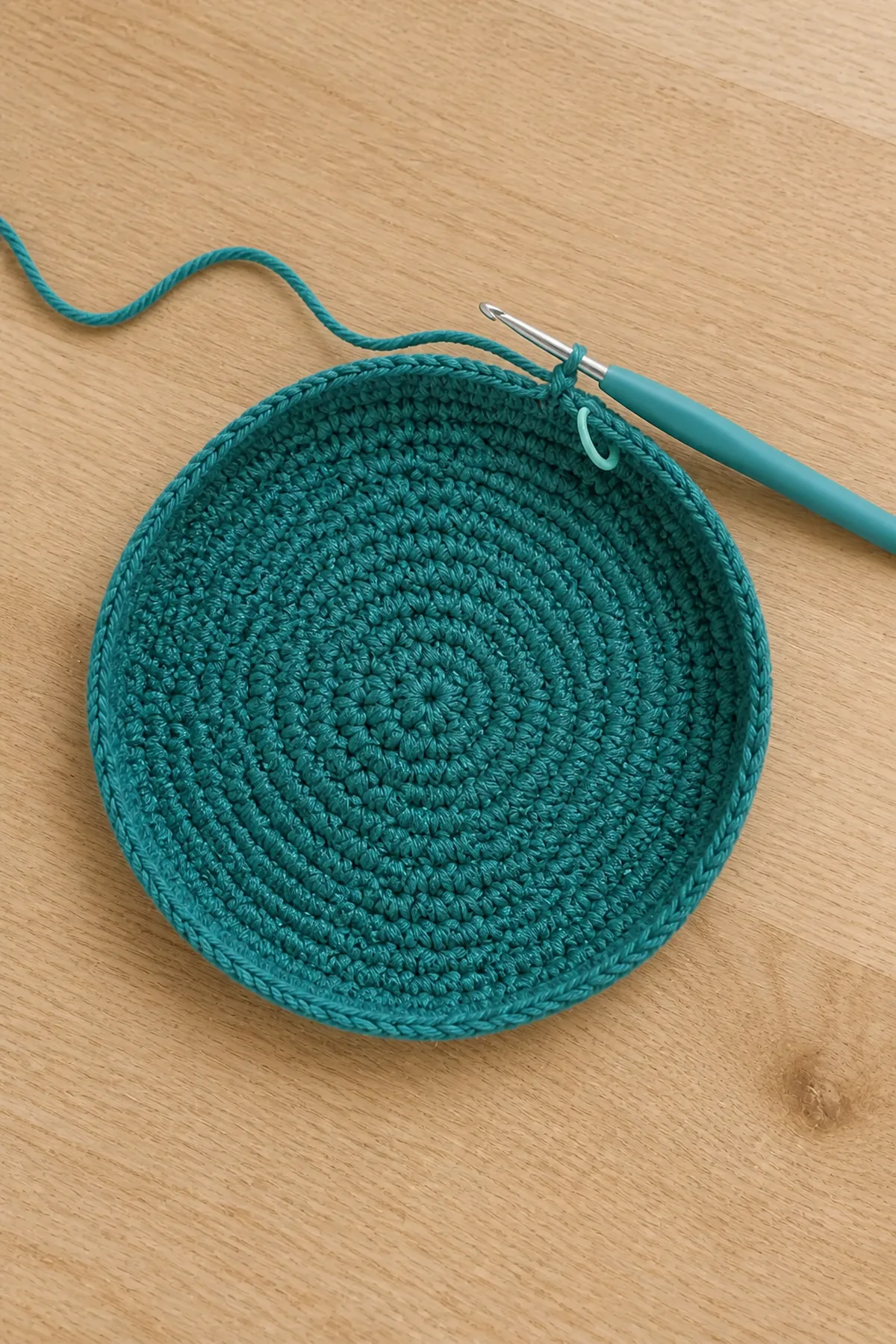 Deep-teal circular crochet bag base beginning to curve upward
