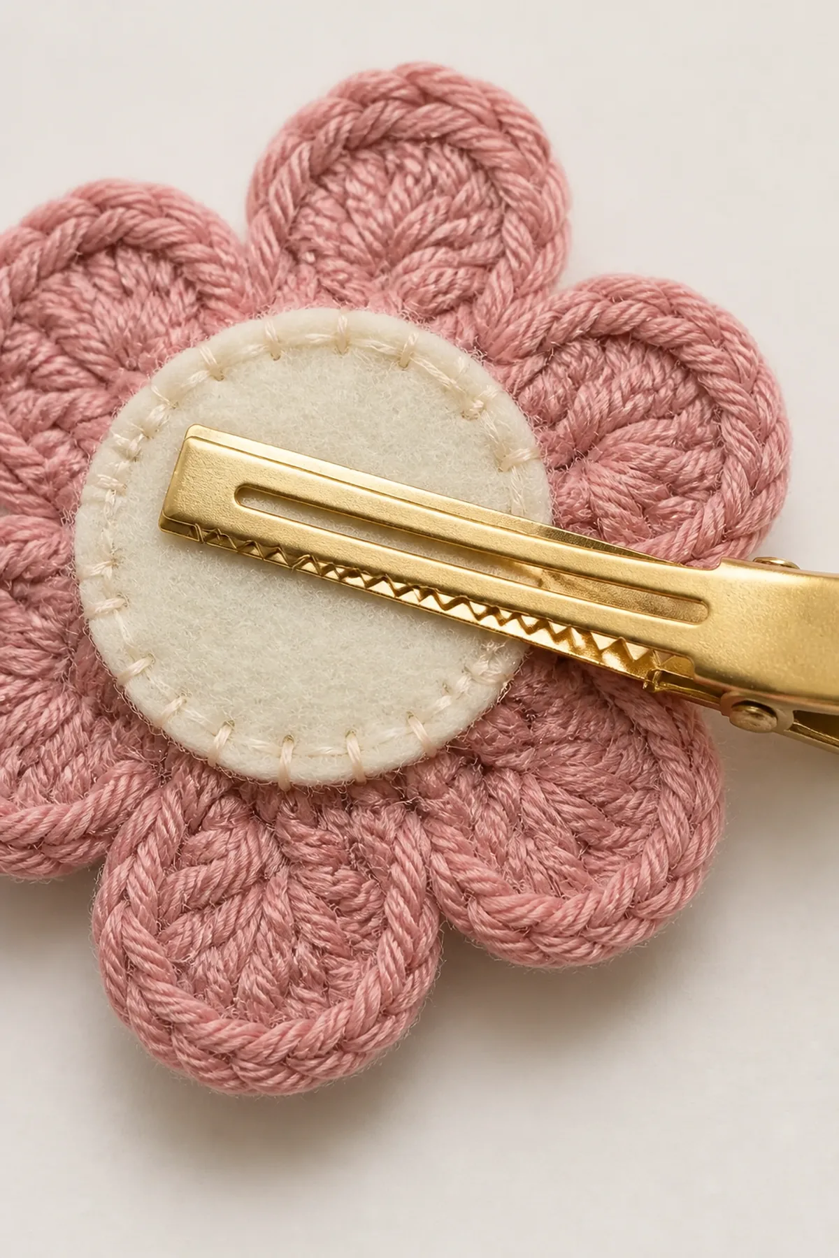 Close-up of neat felt stitches securing a gold clip to a dusty-pink crochet flower