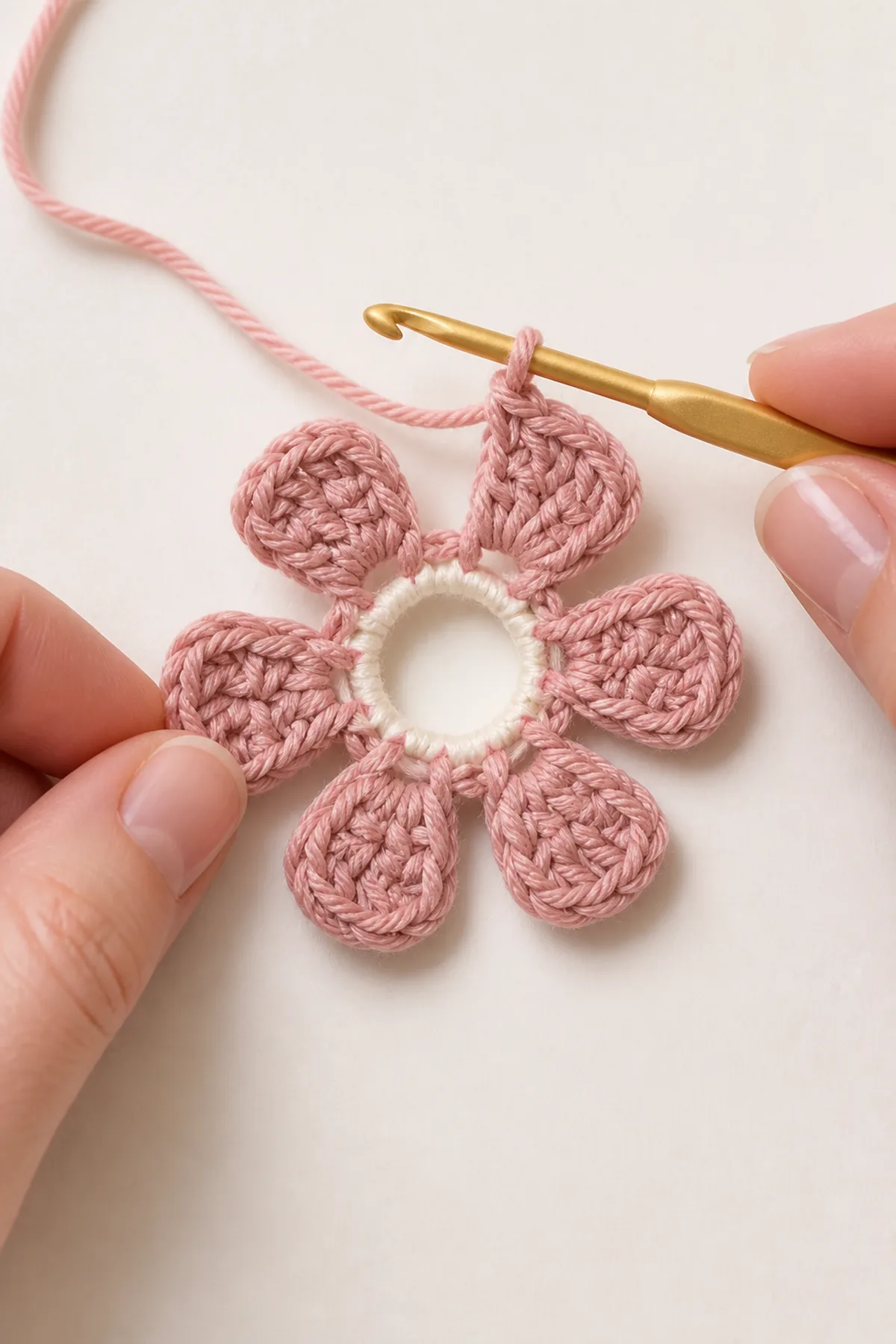 Dusty-pink six-petal crochet flower being worked around a cream center