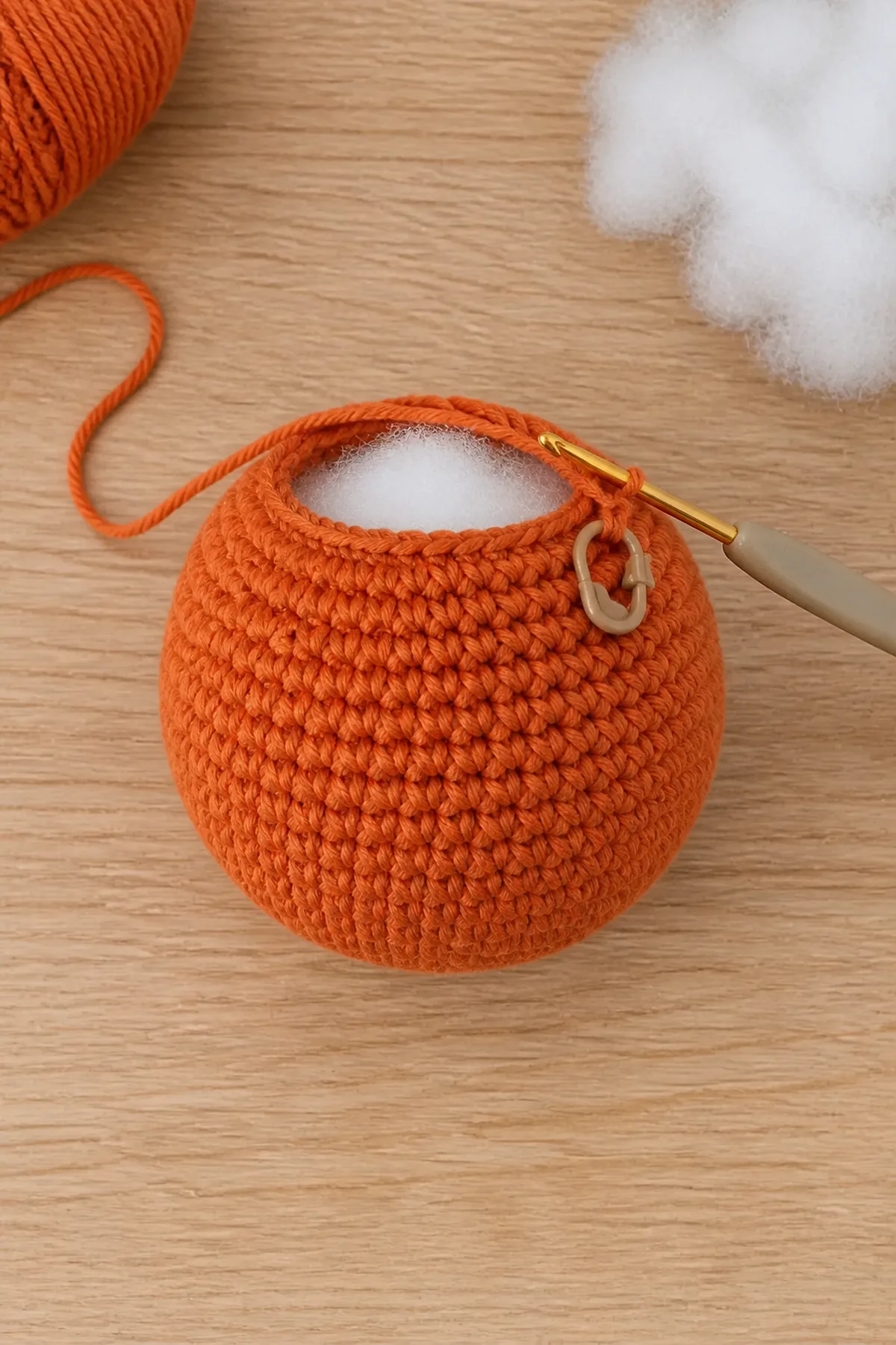 Partially crocheted orange pumpkin sphere being stuffed before the decrease rounds